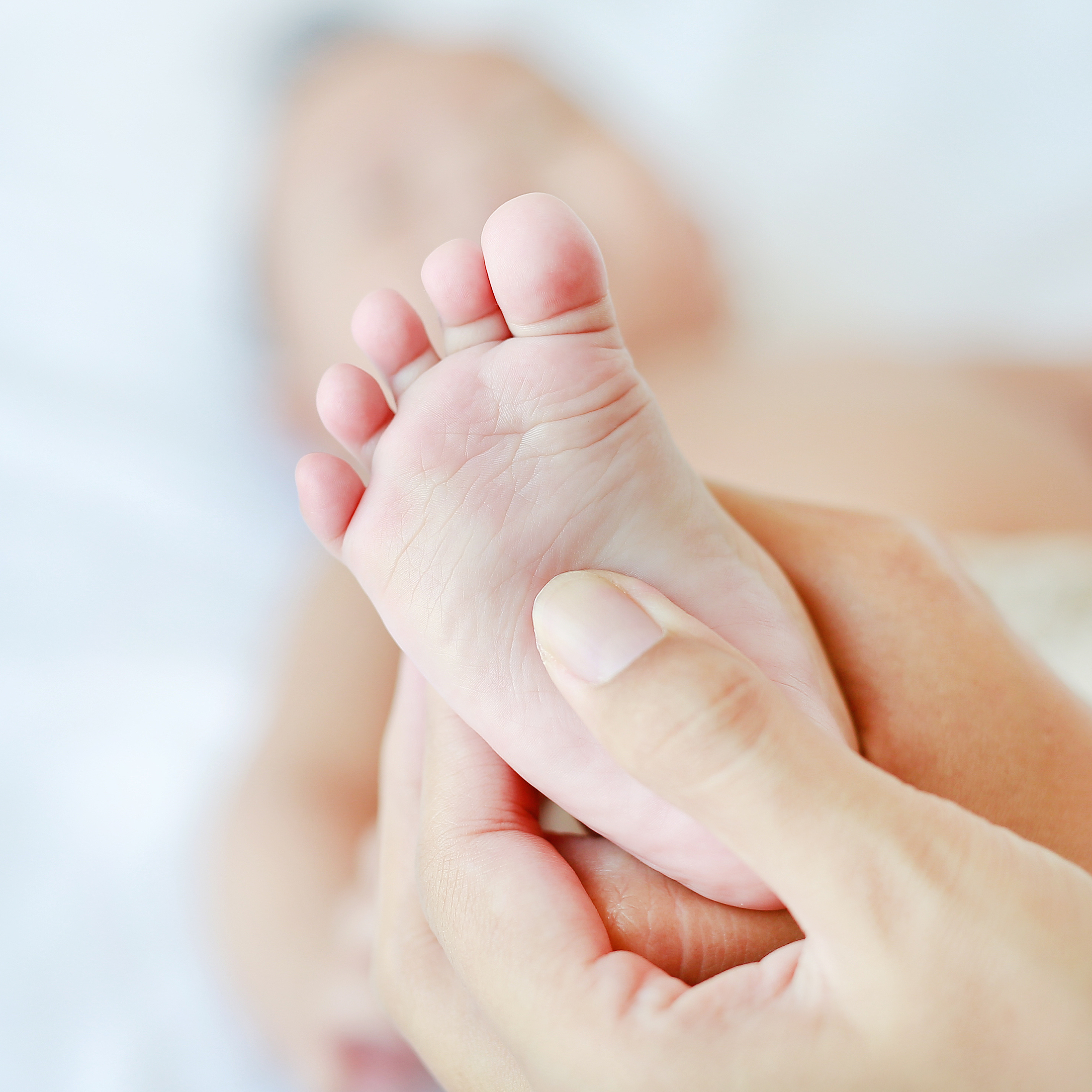 Hand einer Physiotherapeutin drückt auf die Sohle eines Babyfusses