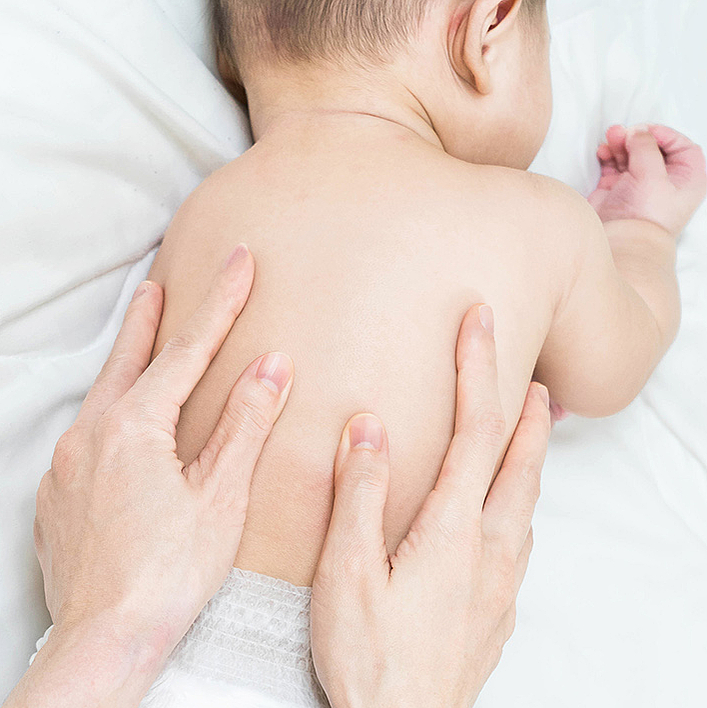 Baby auf dem Bauch liegend, Händer der Therapeutin auf dem Rücken